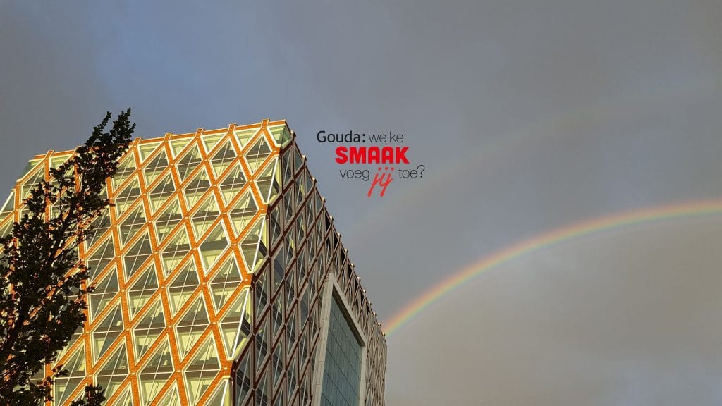 Zijaanzicht van het Huis van de Stad met rechts ervan een regenboog. In het midden het logo Gouda: welke smaak voeg jij toe?